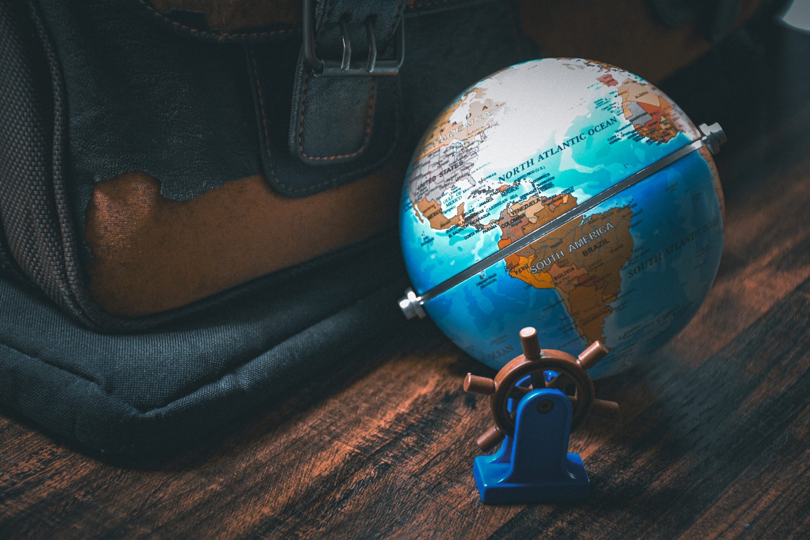 Mock-up globe showing a map of America and a model ship's steering wheel on a background of a wooden table and a classic suitcase in vintage tones.